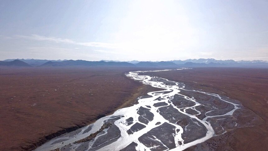 A river winds through a wide tundra with mountains in the distance.