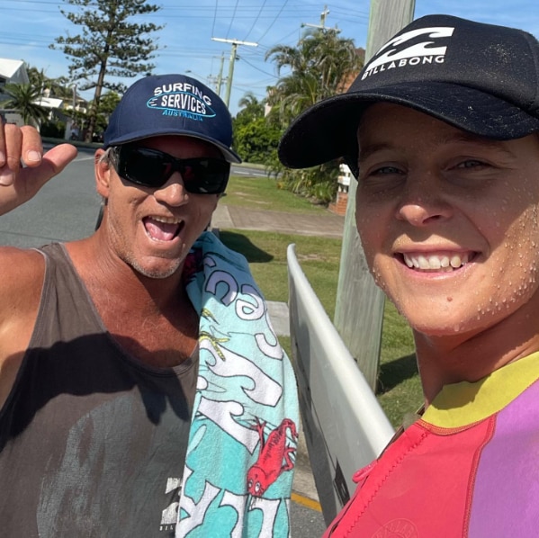 A woman takes a selfie with a man waving his hand