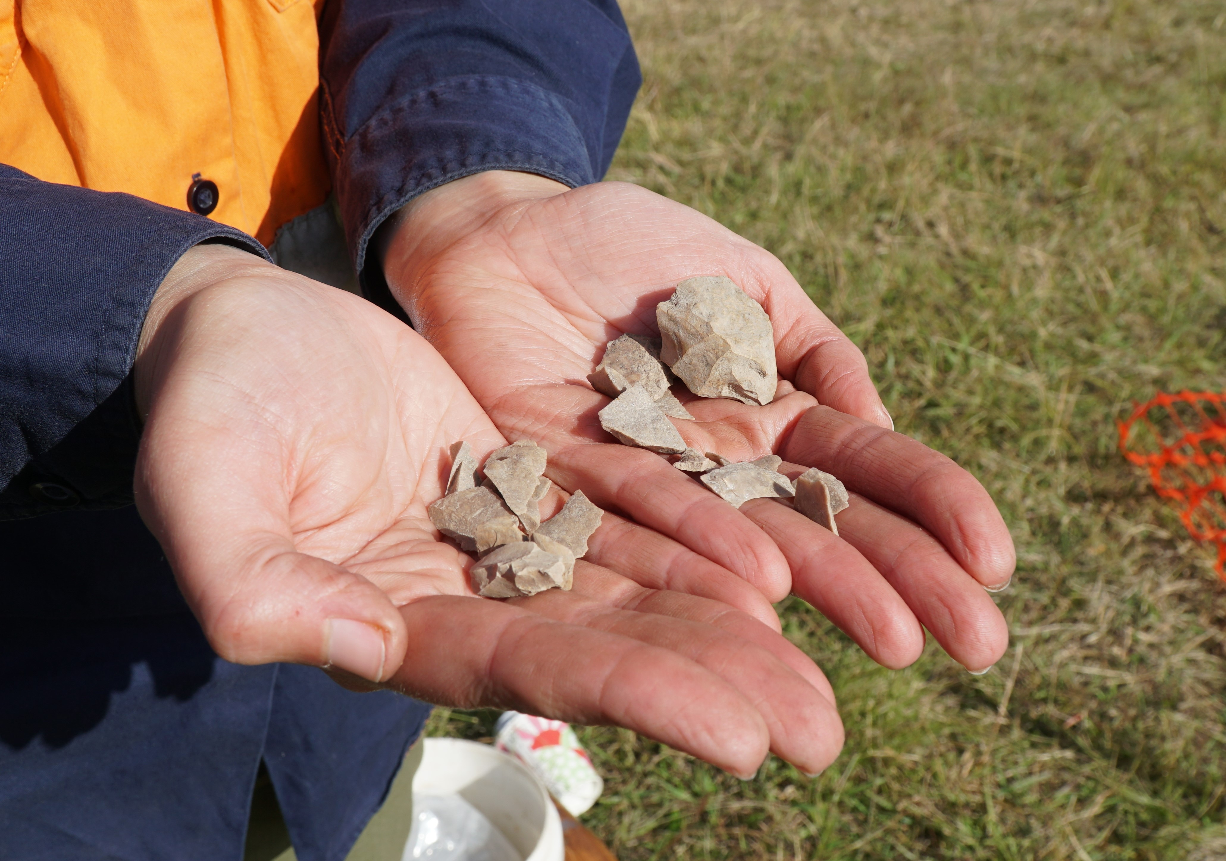 Two cupped hands hold a number of indigenous artefacts. 
