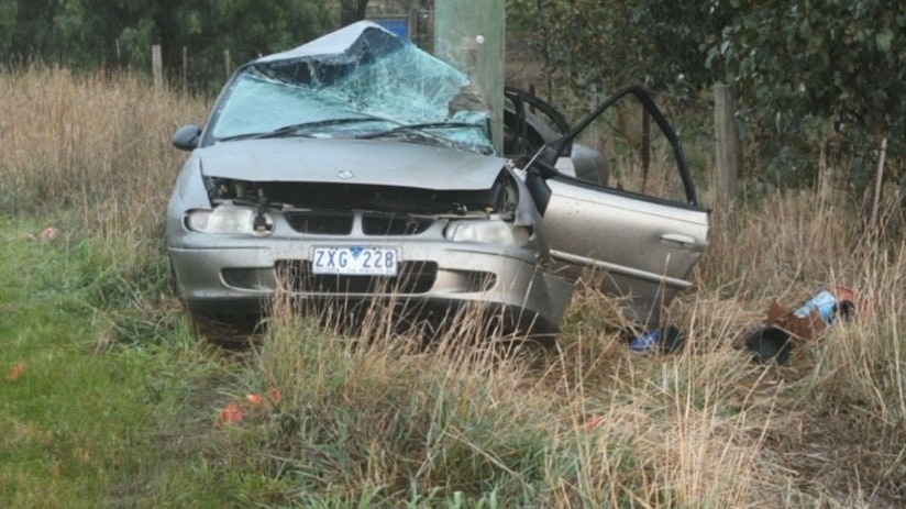 A wrecked car crashed into a power pole with a smashed windscreen and open passenger door.