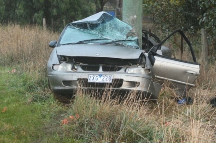 A wrecked car crashed into a power pole with a smashed windscreen and open passenger door.