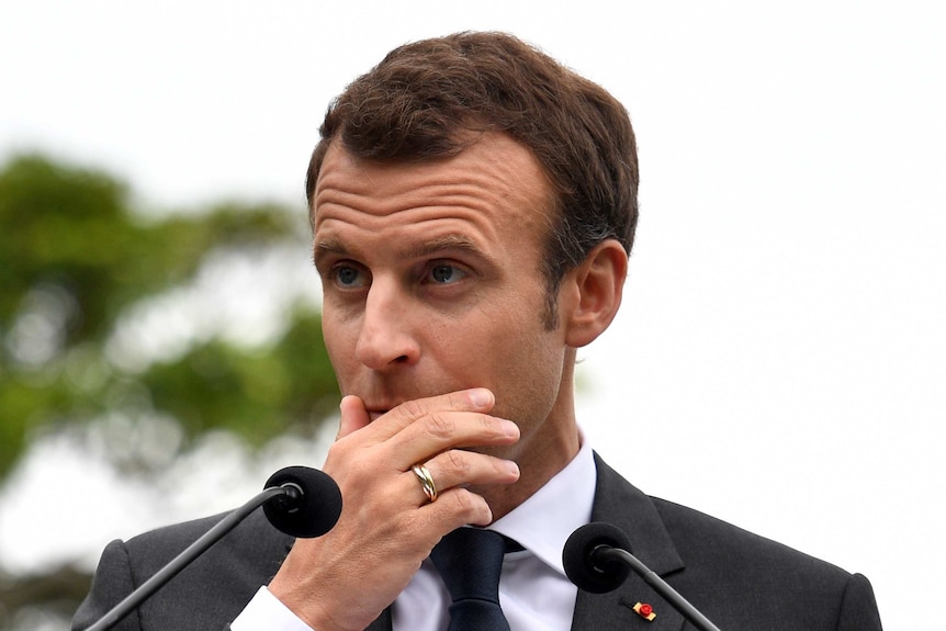 President of France Emmanuel Macron has his hand over his mouth during a press conference.