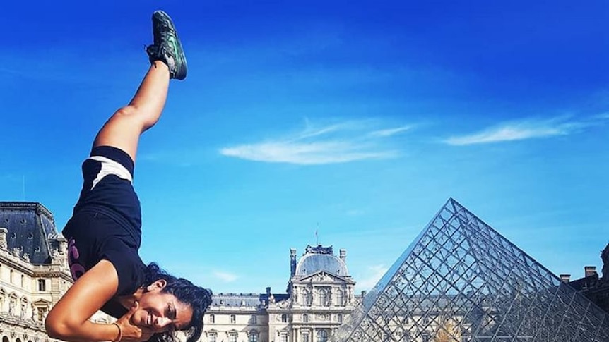 One-legged woman performing one-handed handstand in front of the Louvre