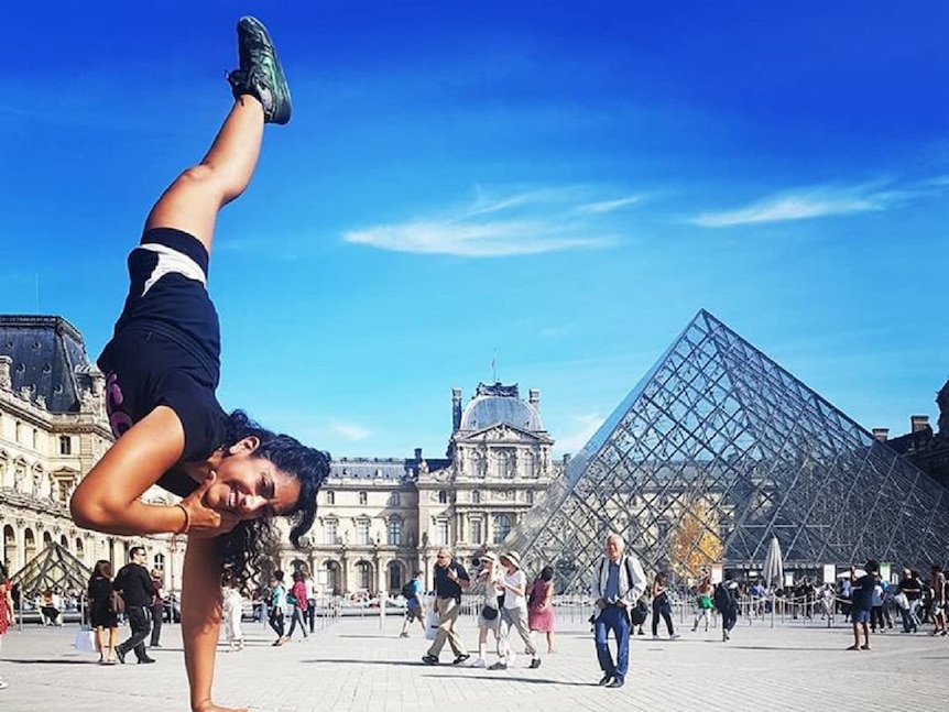 One-legged woman performing one-handed handstand in front of the Louvre