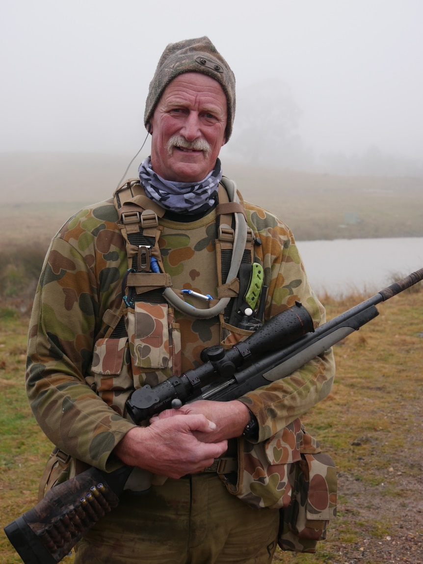 A man holding a gun in camouflage clothing.