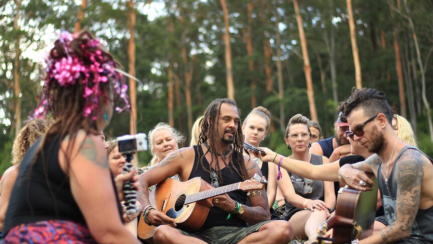 Michael Franti sits on the hill in Woodfordia strumming a tune for adoring fans.