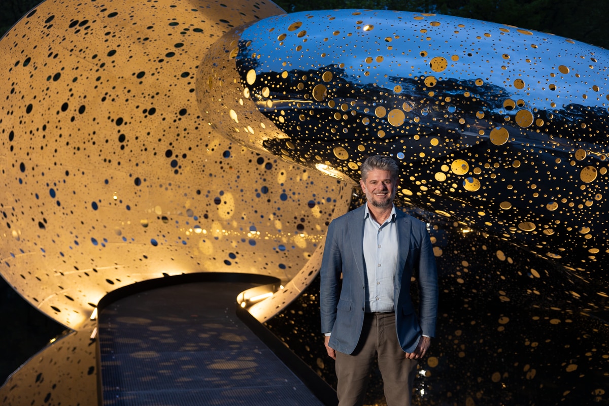A man in a suit stands in front of a twisting silver sculpture.