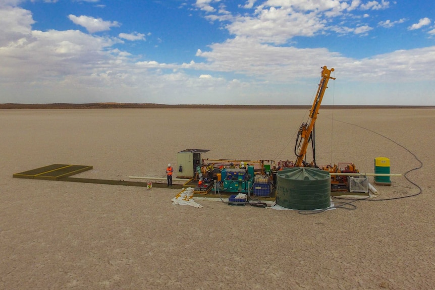 a small drilling platform sits in the middle of a white expanse.  The sky is blue and a man stands on the platform