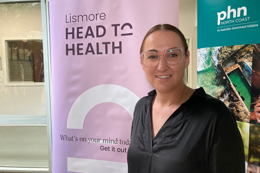 Woman in black shirt,wearing glasses standing in front of a pink banner that reads 'head to health'