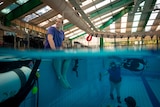 Man sitting on edge of pool, woman underwater wearing scuba gear