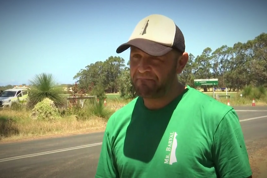 Un homme en casquette et chemise verte debout sur le bord d'une route.