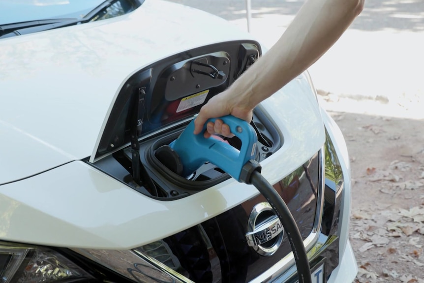 A hand pushes an electric cord into a car.