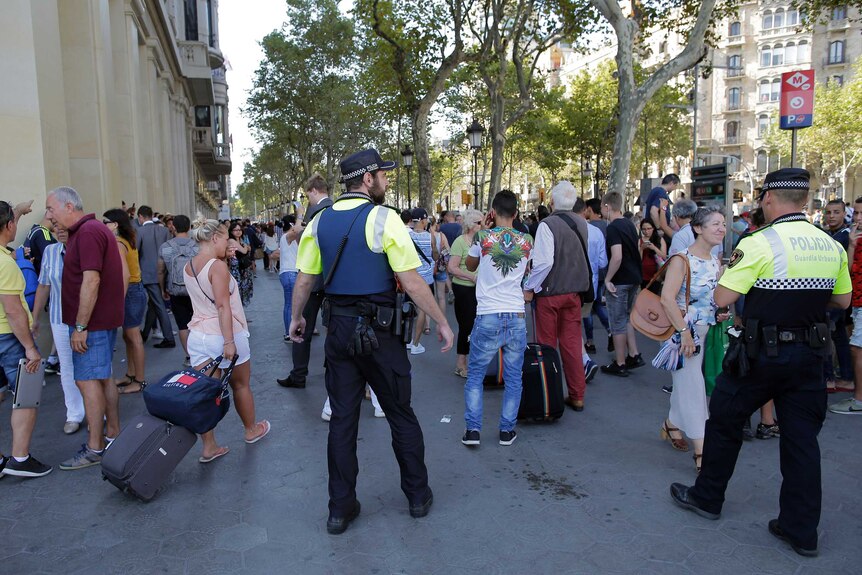 Police officers control a crowd of people standing around.