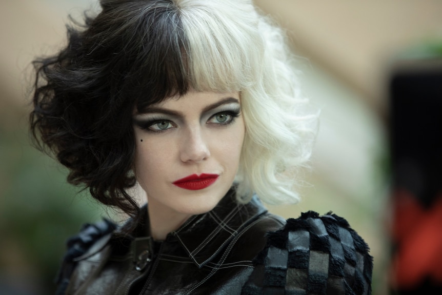 Film still of Emma Stone as Cruella in close-up, wearing red lipstick and Cruella's signature black and white two-tone hair