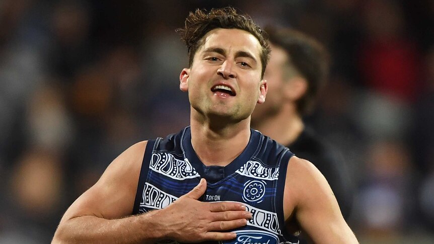 A male AFL play taps his chest as he celebrates kicking a goal for the Cats.