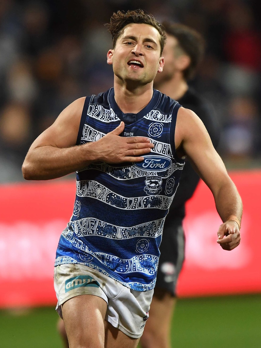 A male AFL play taps his chest as he celebrates kicking a goal for the Cats.