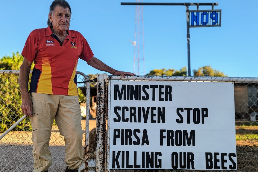 An elderly fair-skinned man, Rob, stands with a sign that reads Minister Scriven Stop PIRSA killing our bees