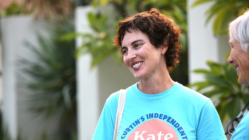 A woman wearing a blue t-shirt smiles. The t-shirt says "Curtin's independent voice, Kate Chaney"