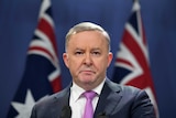 Anthony Albanese stands before two flags