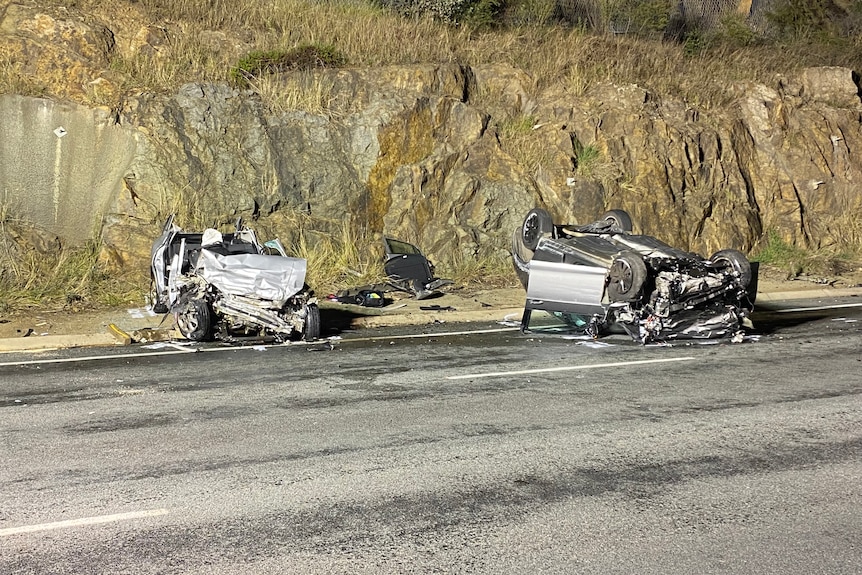 Wreckage of two cars, one which is on its roof, on a road after a crash.