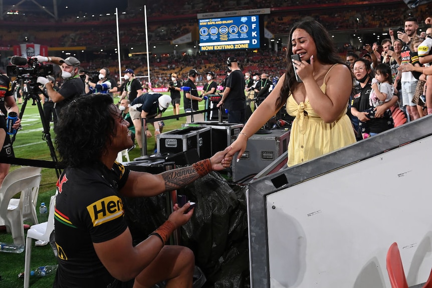penrith panthers player brian to'o is down on one knee proposing to his partner. she is crying and wearing a pale yellow dress