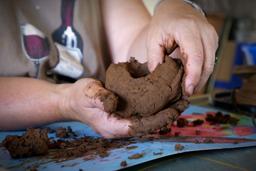 A close up of a woman's hands molding sticky brown clay