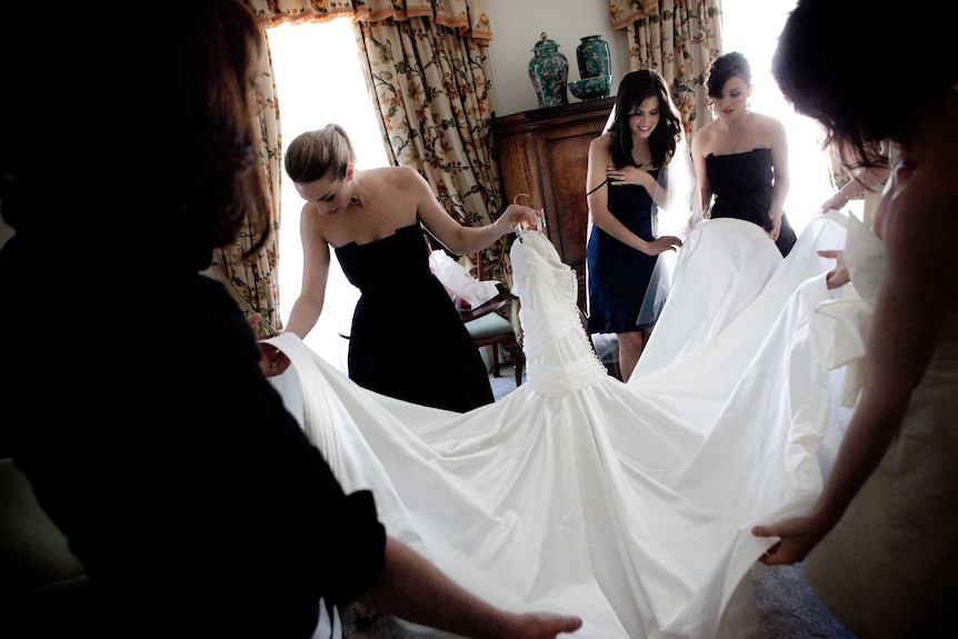 Three pretty women in black dresses prepare a wedding dress for a bride