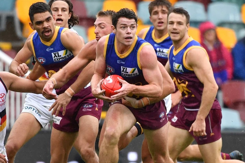 A Brisbane Lions AFL player runs with the ball in both hands in front of his teammates against the Adelaide Crows.