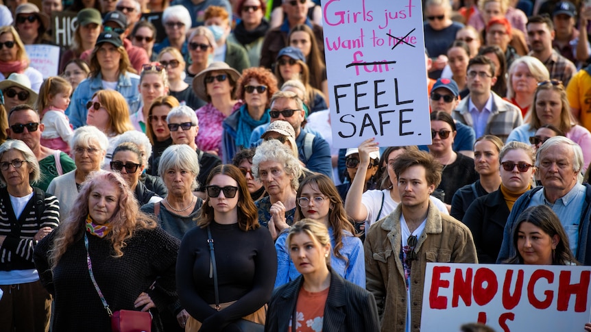 A large group of people gathers for a rally one sign says girls just want to feel safe