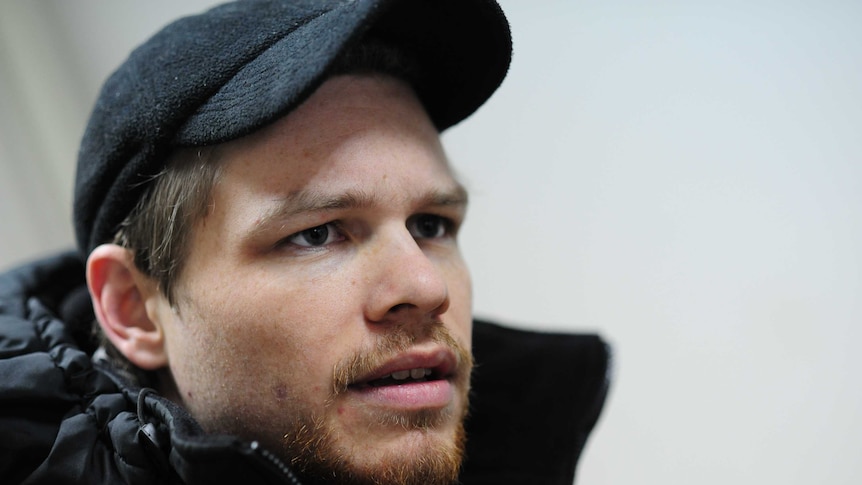 A man with a goatee and wearing a hat has a serious expression on his face