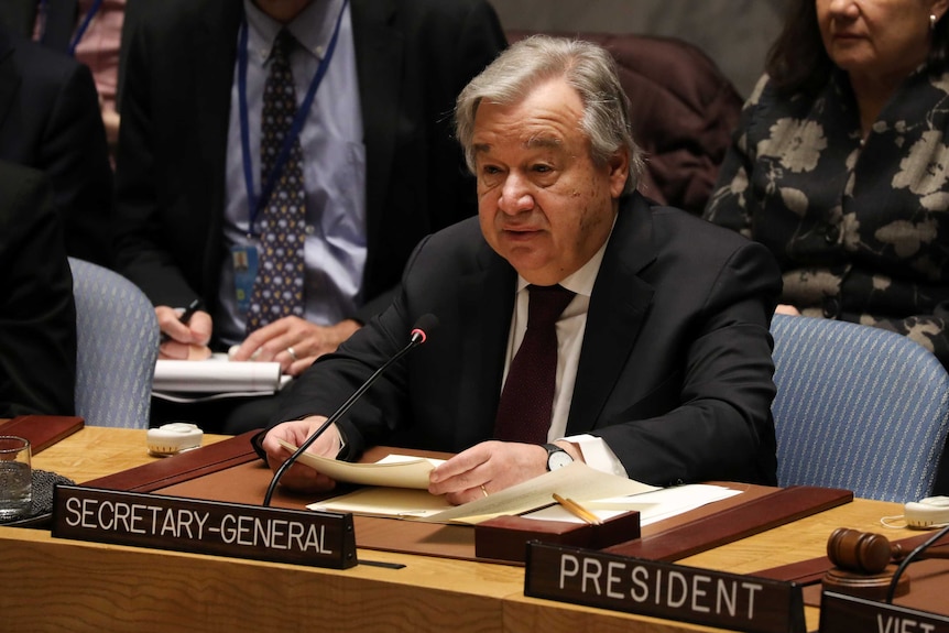 UN Secretary-General Antonio Guterres sitting at a desk behind a small microphone.