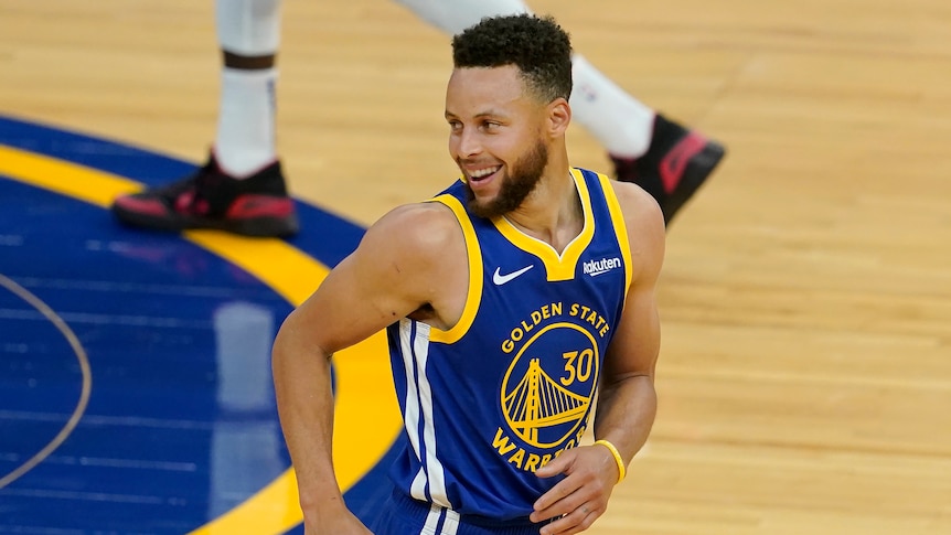 A Golden State Warriors NBA player smiles as he runs down the court.