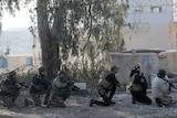 Iraqi men with gun crouch with guns, buildings and trees in the background