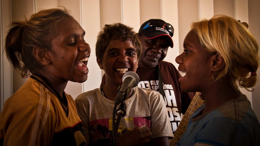 Three young Aboriginal girls singing into microphone.