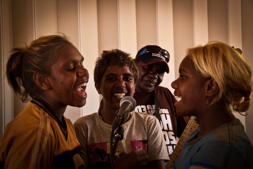 Three young Aboriginal girls singing into microphone.