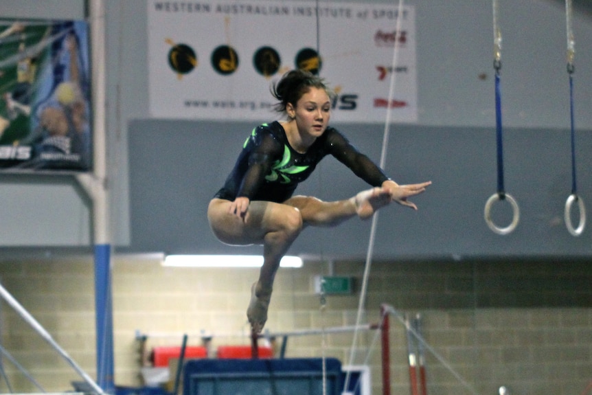 A girl doing a mid-air high kick in a gymnasium.