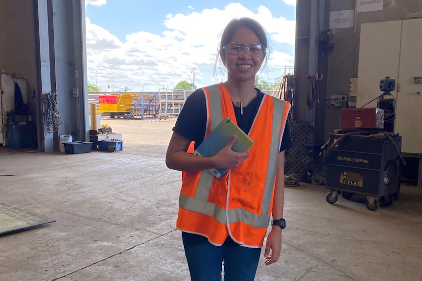 a young woman in a high vis shirt in a shed smiles at the camera