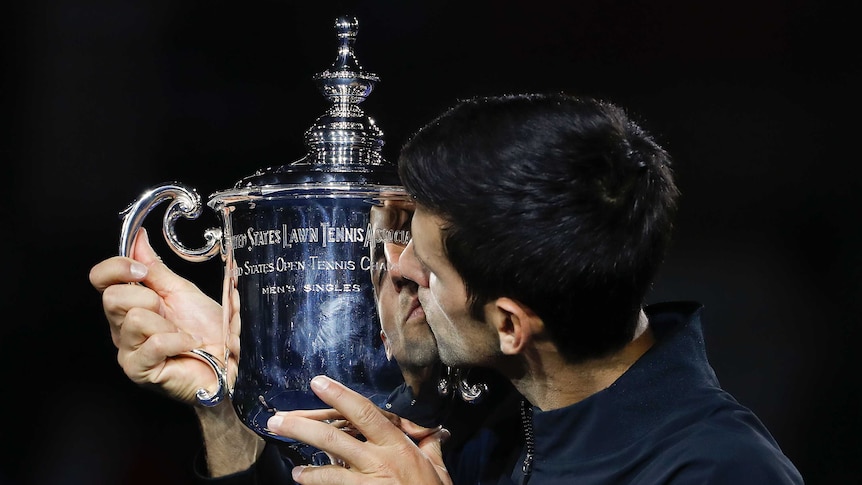 Novak Djokovic kisses a large silver cup.