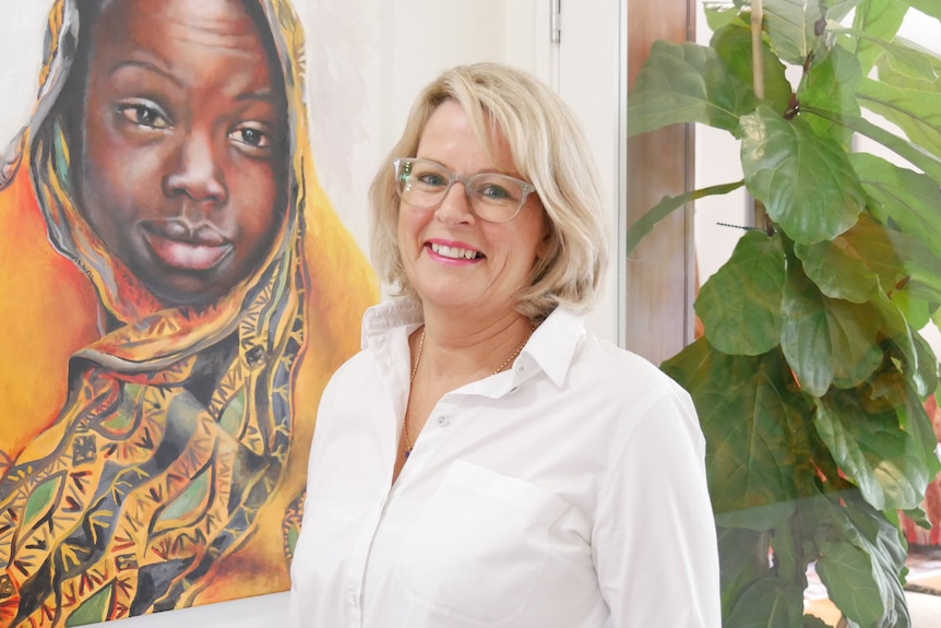 A blonde haired woman stands in front of a poster of an African child