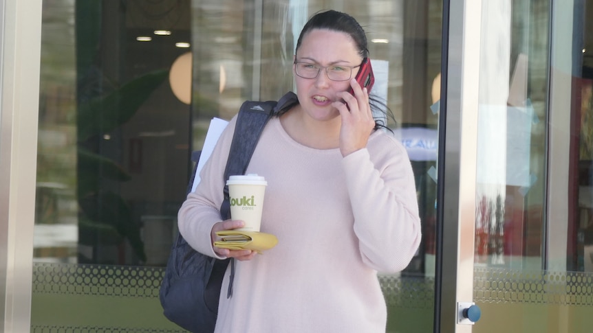A woman talks on a mobile phone while holding a coffee and banana in her other hand.