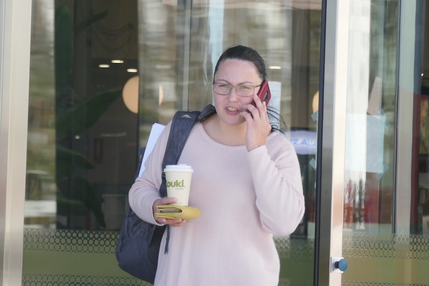 A woman talks on a mobile phone while holding a coffee and banana in her other hand.