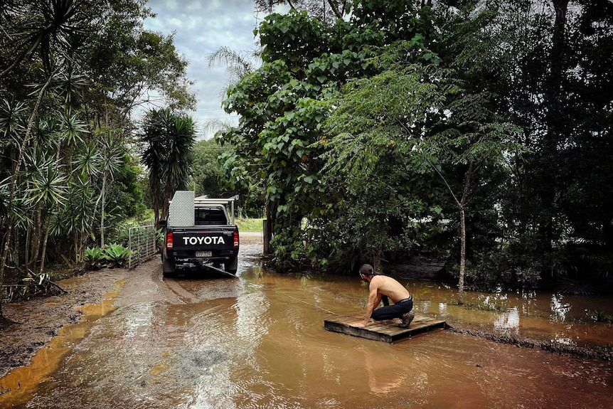 man weighing down timber raft, behind pulled behind a ute