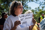Indigenous woman holding sign that reads 'Lord Jesus set Yarrabah free'.