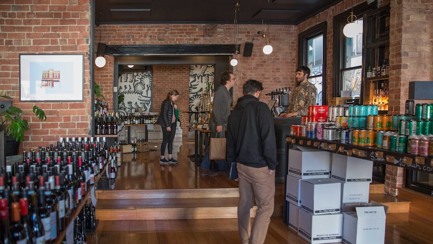 Three customers browse wine and beer inside the brick shop