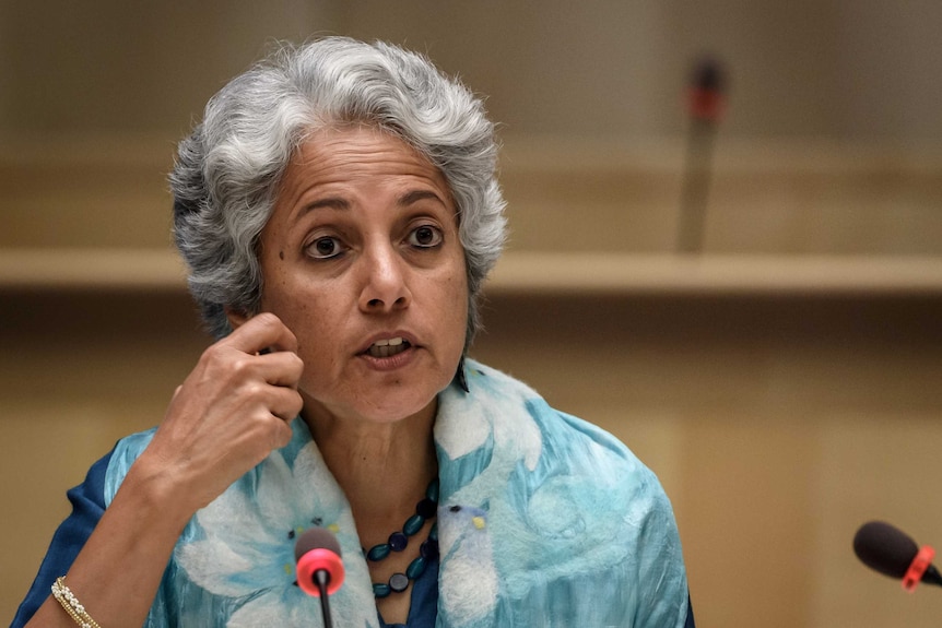 A woman with grey hair gestures at a microphone.