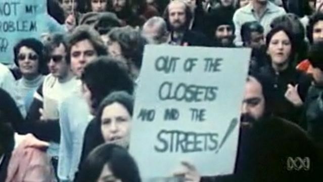 A protest crowd, protest sign reads: "Out of the closets and into the streets!"