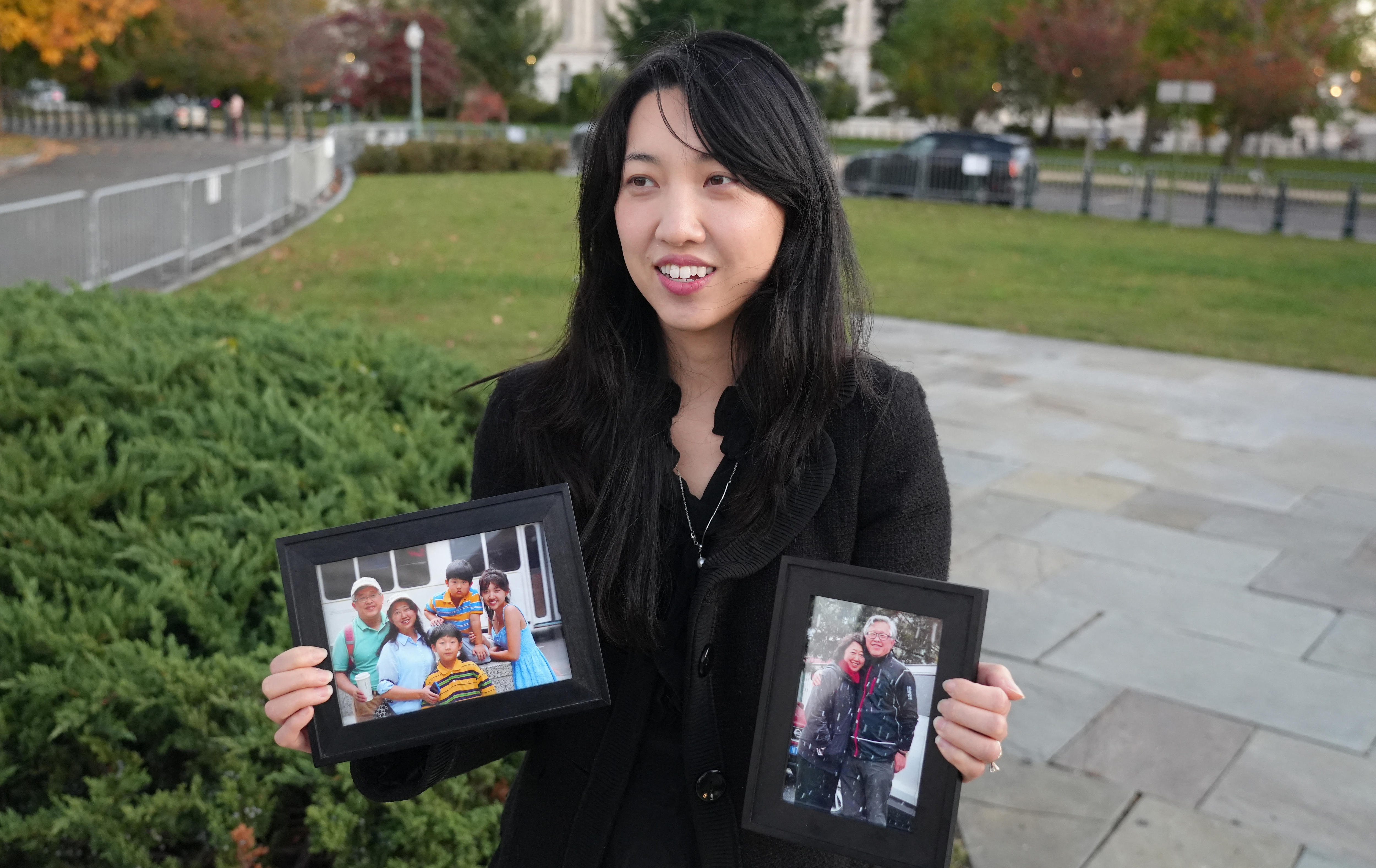 Uma mulher com longos cabelos escuros segura um par de fotos de família em um parque.
