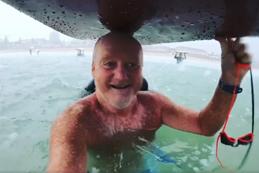 A man sheltering under a surfboard during a storm