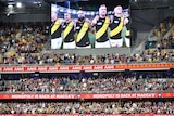 Richmond players are seen standing shoulder to shoulder on a big screen in front of a large crowd