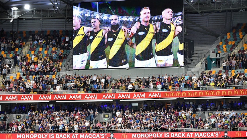 Richmond players are seen standing shoulder to shoulder on a big screen in front of a large crowd